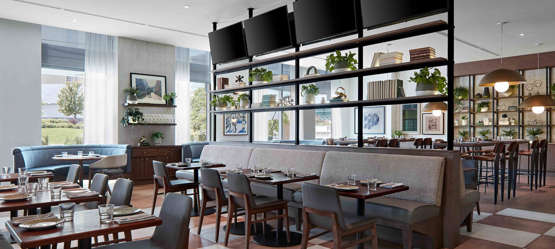 Spacious restaurant dining room with elegant booth seating, wood tables, and natural light through large windows.