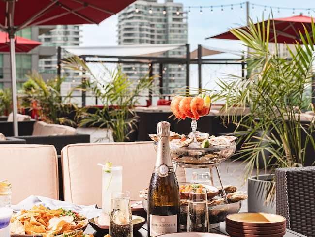Toronto skyline behind a seafood tower and champagne during a sunny rooftop celebration at Bar Caña