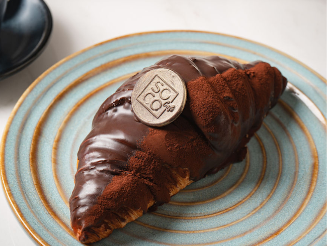 Close-up of a flaky chocolate croissant on a green ceramic plate.
